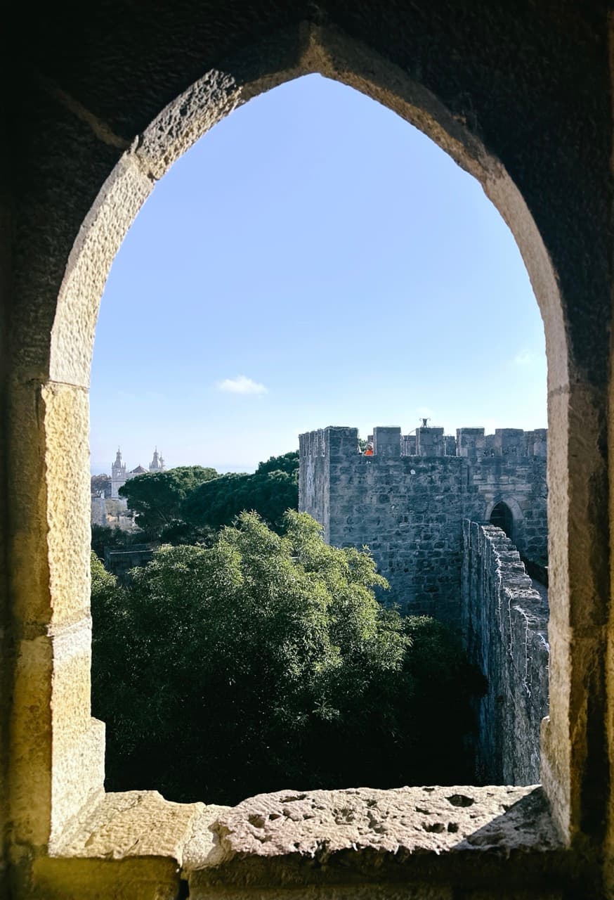 Castle ramparts and distant church towers seen through a pointed stone archway window