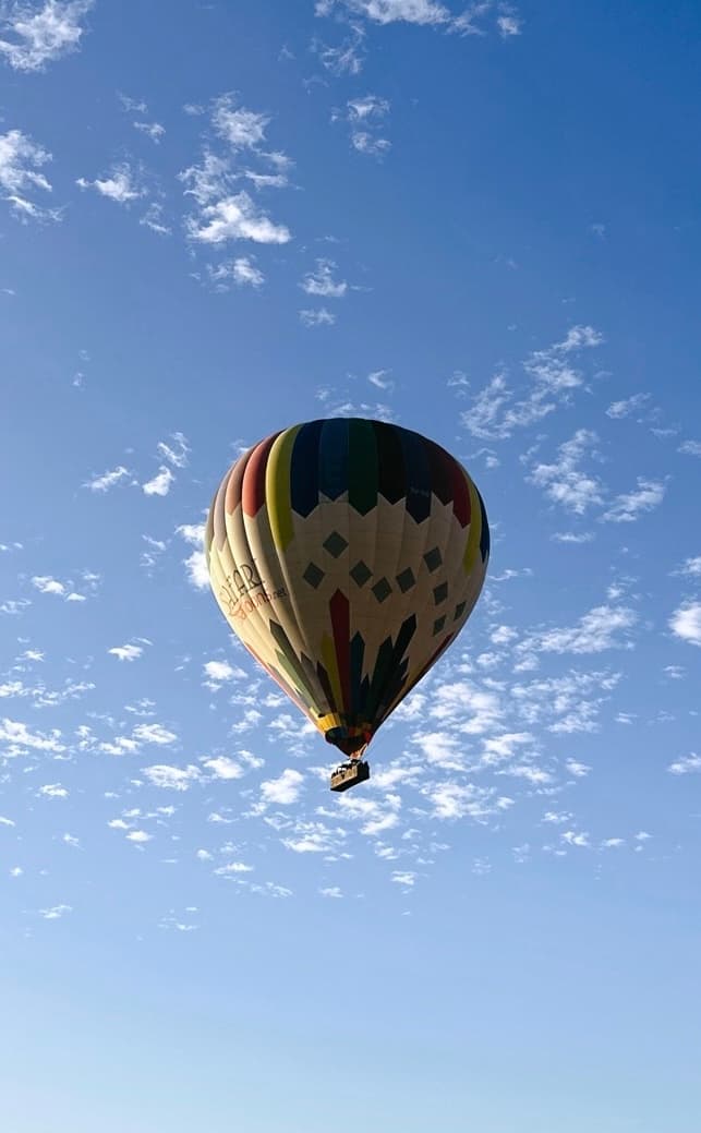A colorfully patterned hot-air balloon drifting in a blue sky scattered with small clouds