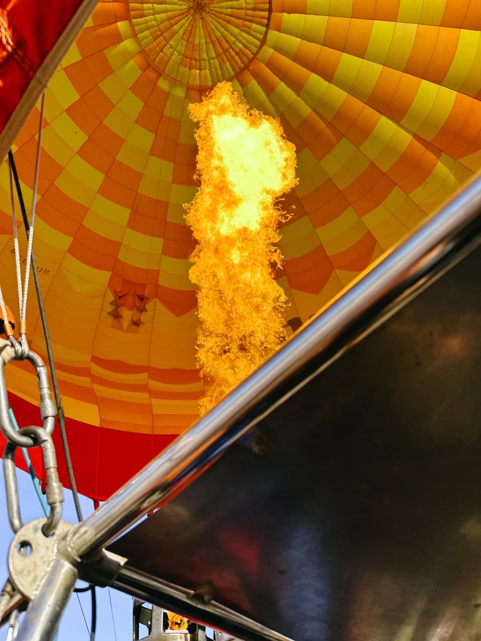 A burner flame roaring up into the yellow-and-orange envelope of a hot-air balloon, seen from the basket